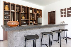 A kitchen with a central island, bar stools, and a wooden shelf unit with various kitchenware.