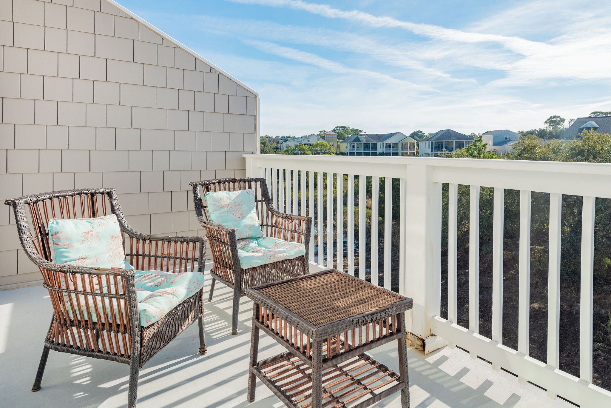 A balcony with wicker furniture and a view of neighboring houses.