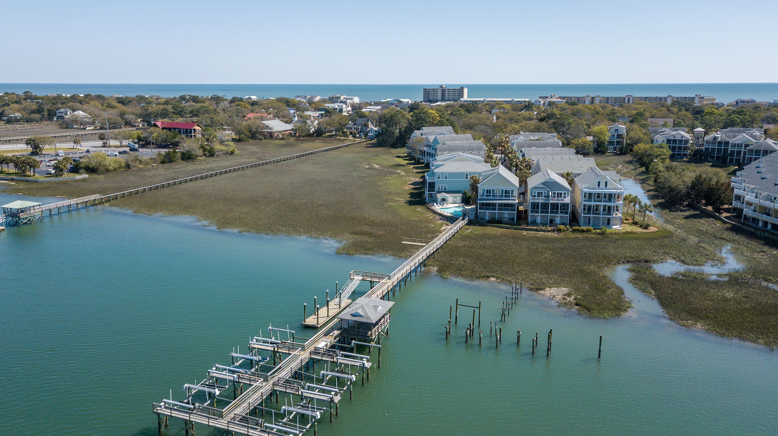 A coastal property with a dock extending into the water, surrounded by residential buildings and a clear view of the ocean.