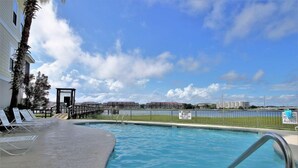 A swimming pool with lounge chairs, a lifeguard station, and a view of distant buildings.