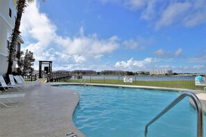 Une piscine avec des chaises longues, un poste de surveillance pour les sauveteurs et une vue sur les bâtiments situés au loin.