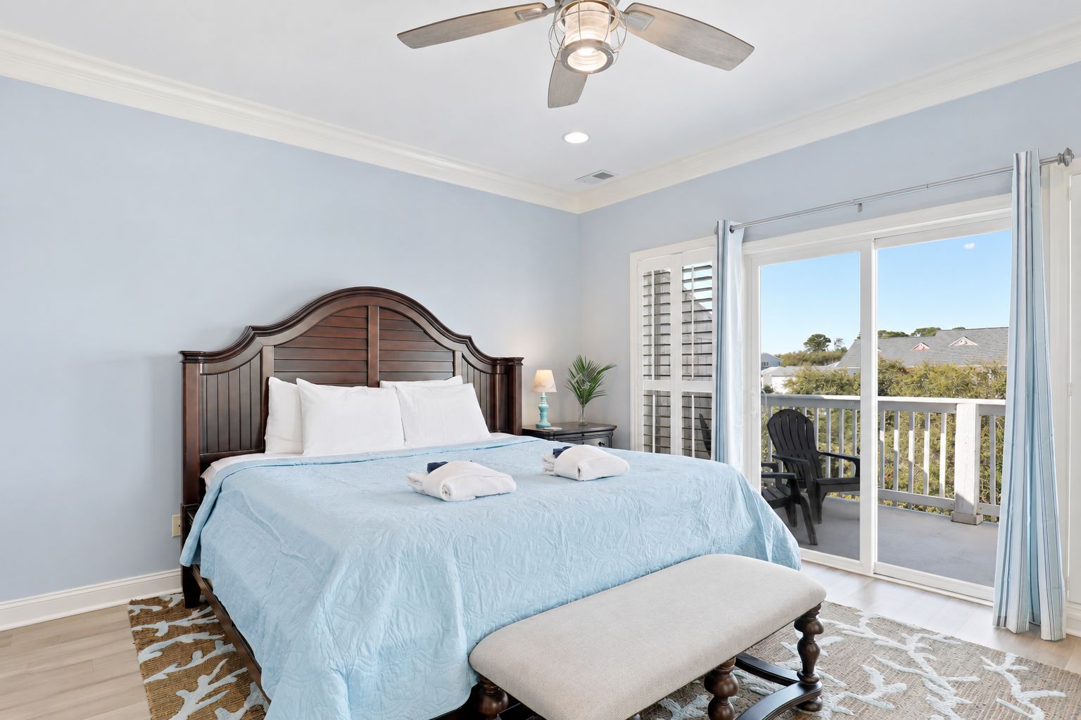A bedroom with a bed, a bench, a ceiling fan, and a view of the outside.