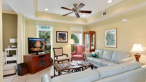 Una sala de estar con ventilador de techo, televisor, sofá, mesa de centro y aparador.