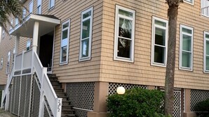Un edificio de varios pisos con un porche cubierto, una escalera y una palmera.