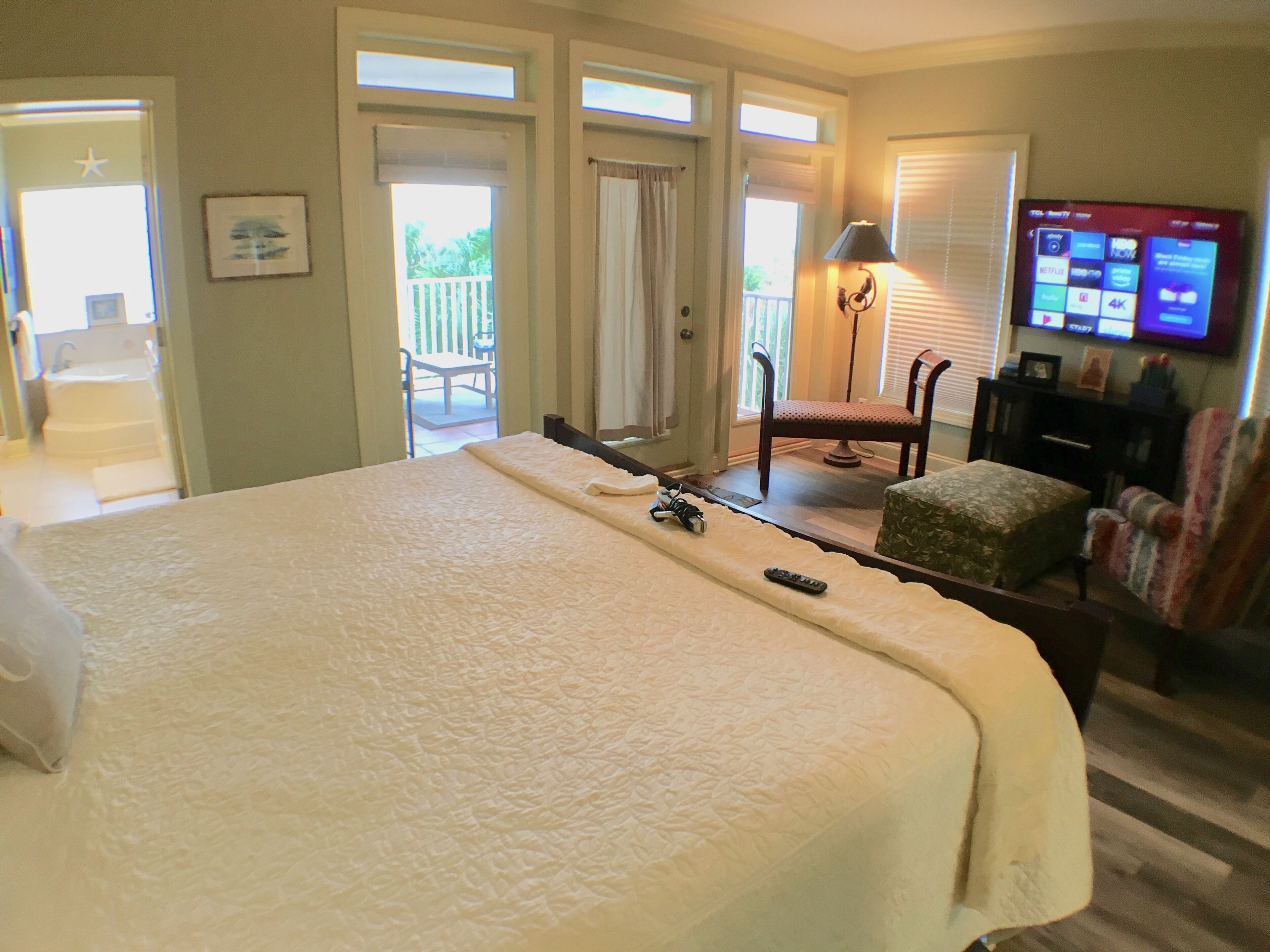A hotel room with a large bed, a chair, a small table, a TV, and a balcony with a view.