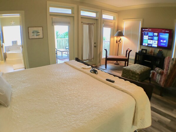 A hotel room with a large bed, a chair, a small table, a TV, and a balcony with a view. - Large Vilano Beach House with heated pool and direct Ocean access. (St Augustine)