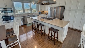 Una cocina moderna con armarios blancos, electrodomésticos de acero inoxidable, una isla grande con taburetes y vistas al exterior por la ventana.