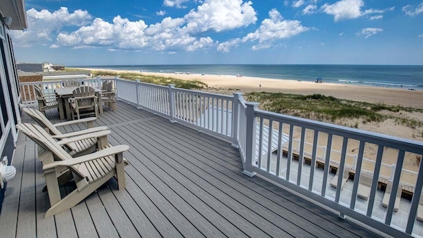 Una terraza de madera con sillas y barandilla que da a una playa.