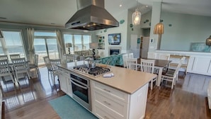 Una cocina amplia con una isla central, muebles de cocina blancos y un gran ventanal con vistas al océano.