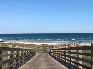 A wooden boardwalk leading to a beach with umbrellas and people. - BOTH BEACH HOUSES-BIG FENCED YARD WITH NO SAND BURS-In Town Near UT Dunes. (Port Aransas)