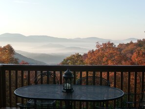 Un balcón con una mesa redonda de metal y sillas, con vistas a un paisaje montañoso con follaje otoñal.