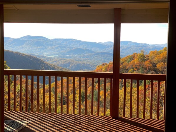 Un balcon en bois offrant une vue sur les arbres aux couleurs automnales et sur des montagnes lointaines.