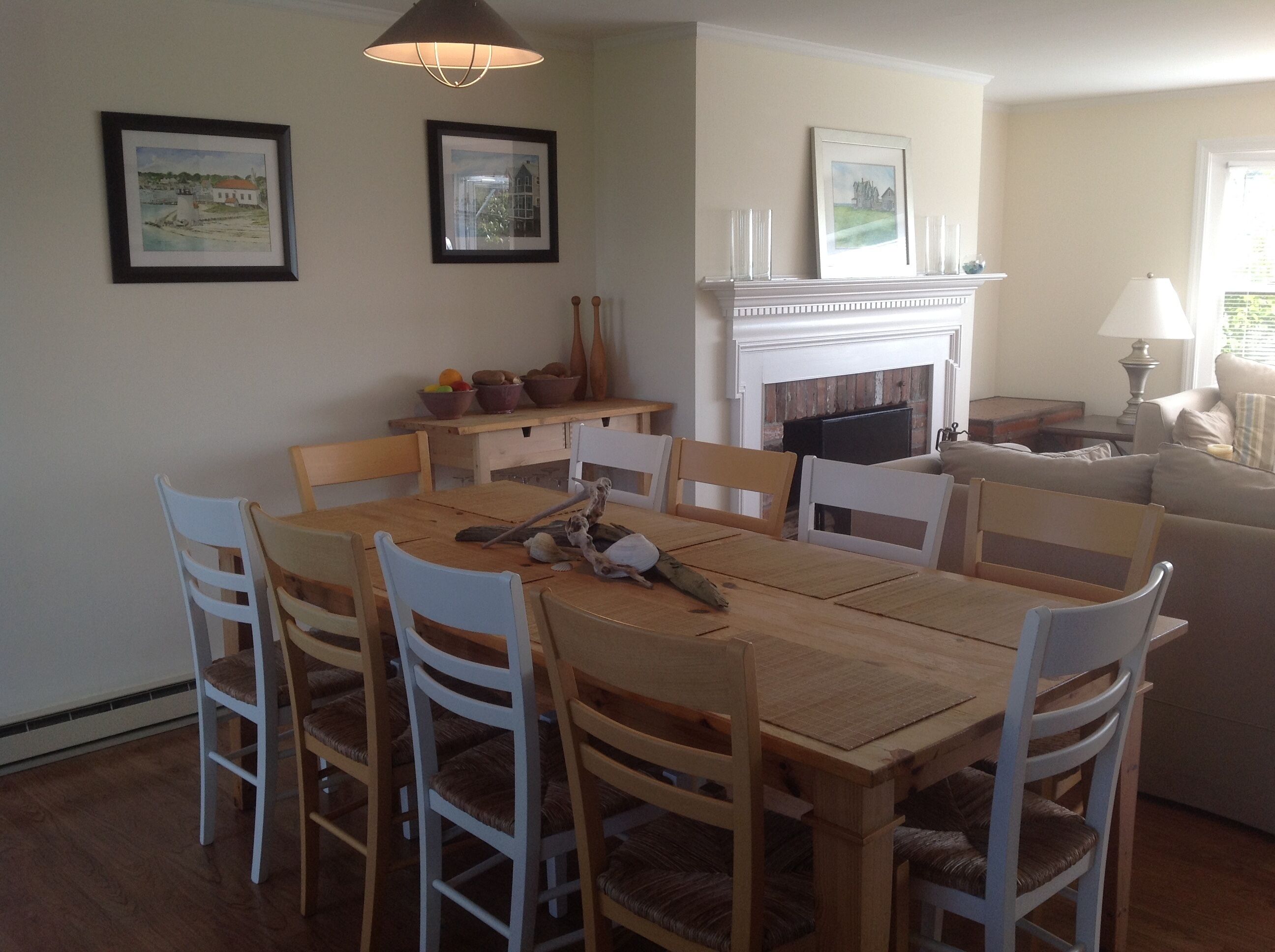 A dining area with a wooden table and white chairs, a fireplace, and framed artwork on the walls.