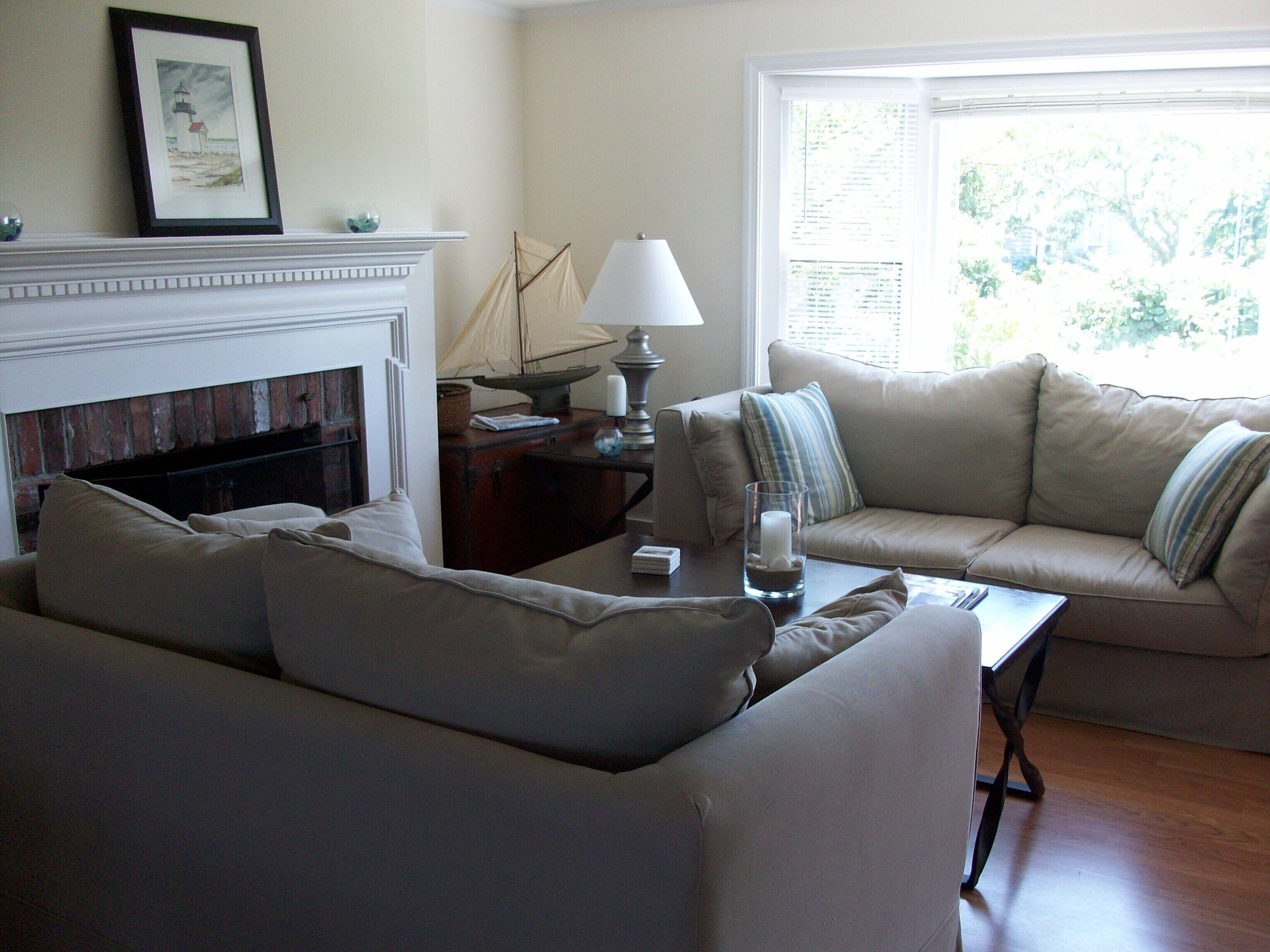 A living room with a fireplace, a sofa, a table with a lamp, and a window with blinds.