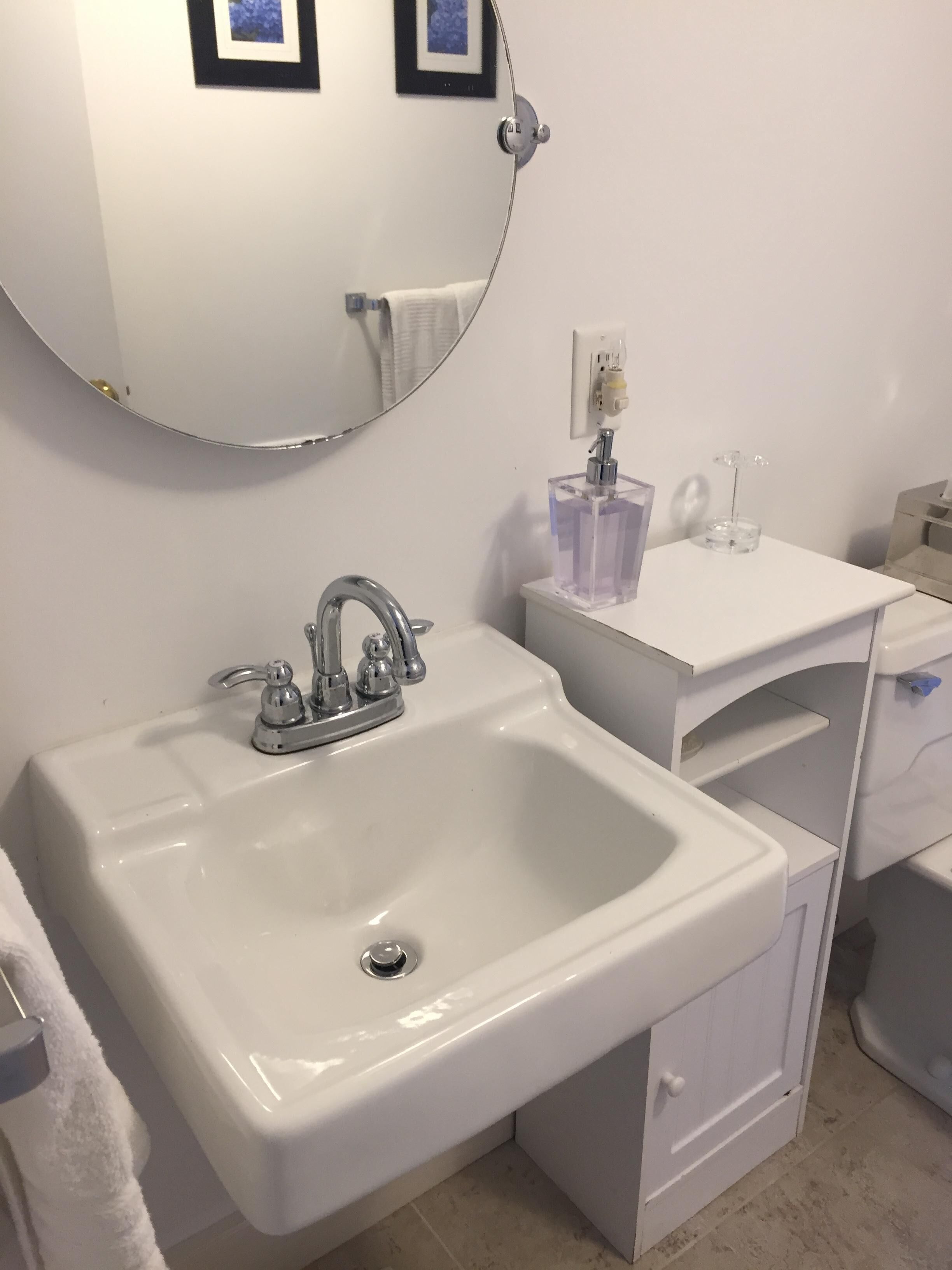 Un bagno con un lavandino bianco, uno specchio rotondo e un mobile vanitario bianco con specchio.