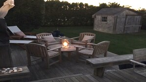 Une terrasse en bois avec une table ronde et des chaises, un petit abri de jardin et une cour gazonnée.