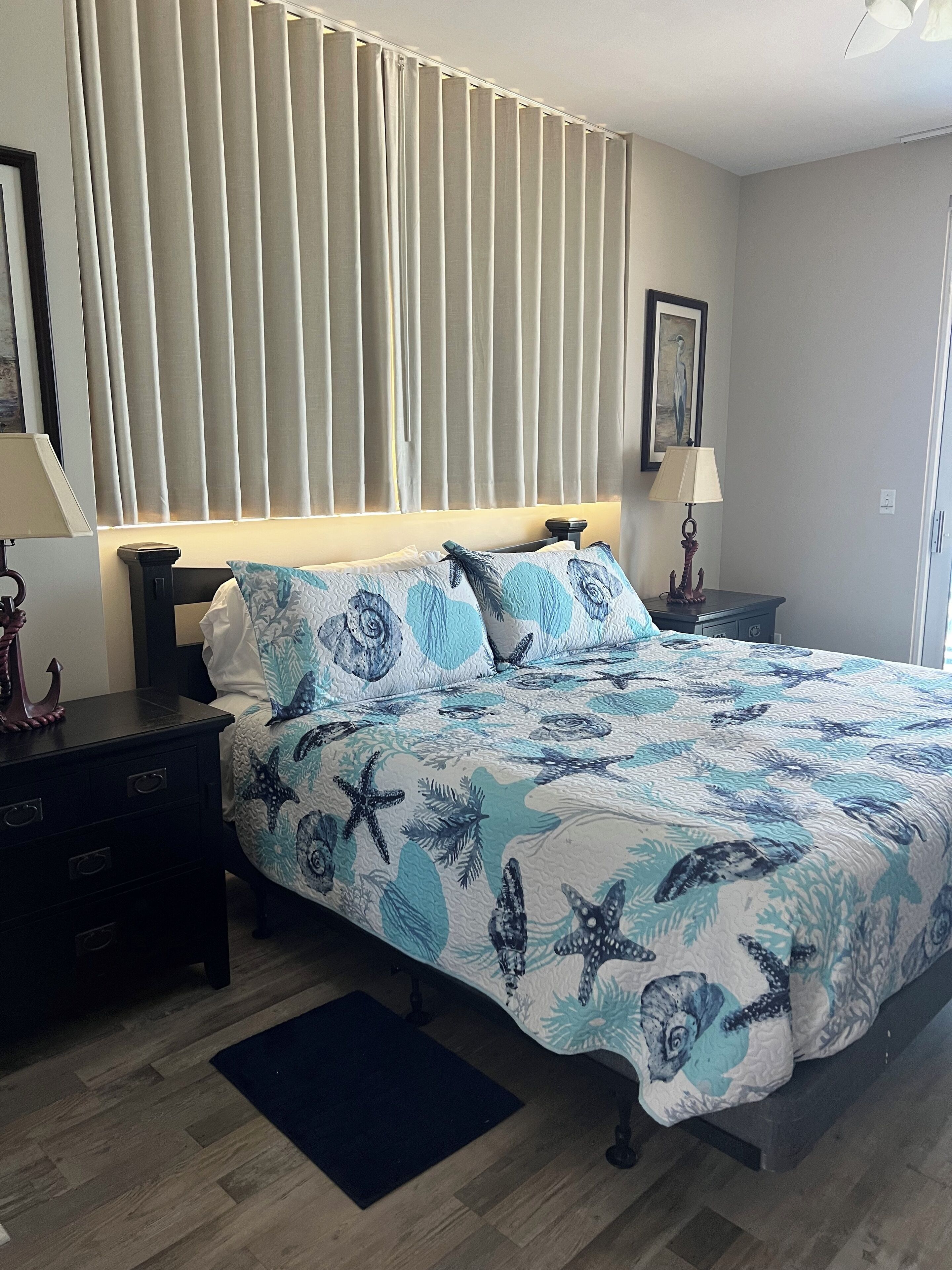Un dormitorio con cama, mesitas de noche, cómoda, ventana con persianas y ventilador de techo.