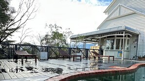 A swimming pool with a brick edge, a wooden deck, and a covered seating area.