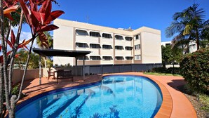 A swimming pool with a tiled edge, surrounded by a patio area with a table and chairs.