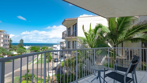 A balcony with a view of the ocean, a table, and chairs.