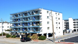Et hotel med flere etager, altaner, parkeringsplads og en klar blå himmel.