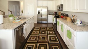 Una cocina con armarios blancos, electrodomésticos de acero inoxidable y un tapete estampado.