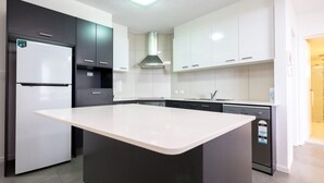 A modern kitchen with a central island, a built-in dishwasher, and a stainless steel range hood. - Pacific Towers Unit 4, 19 Ormonde Tce Kings Beach (KINGS BEACH)