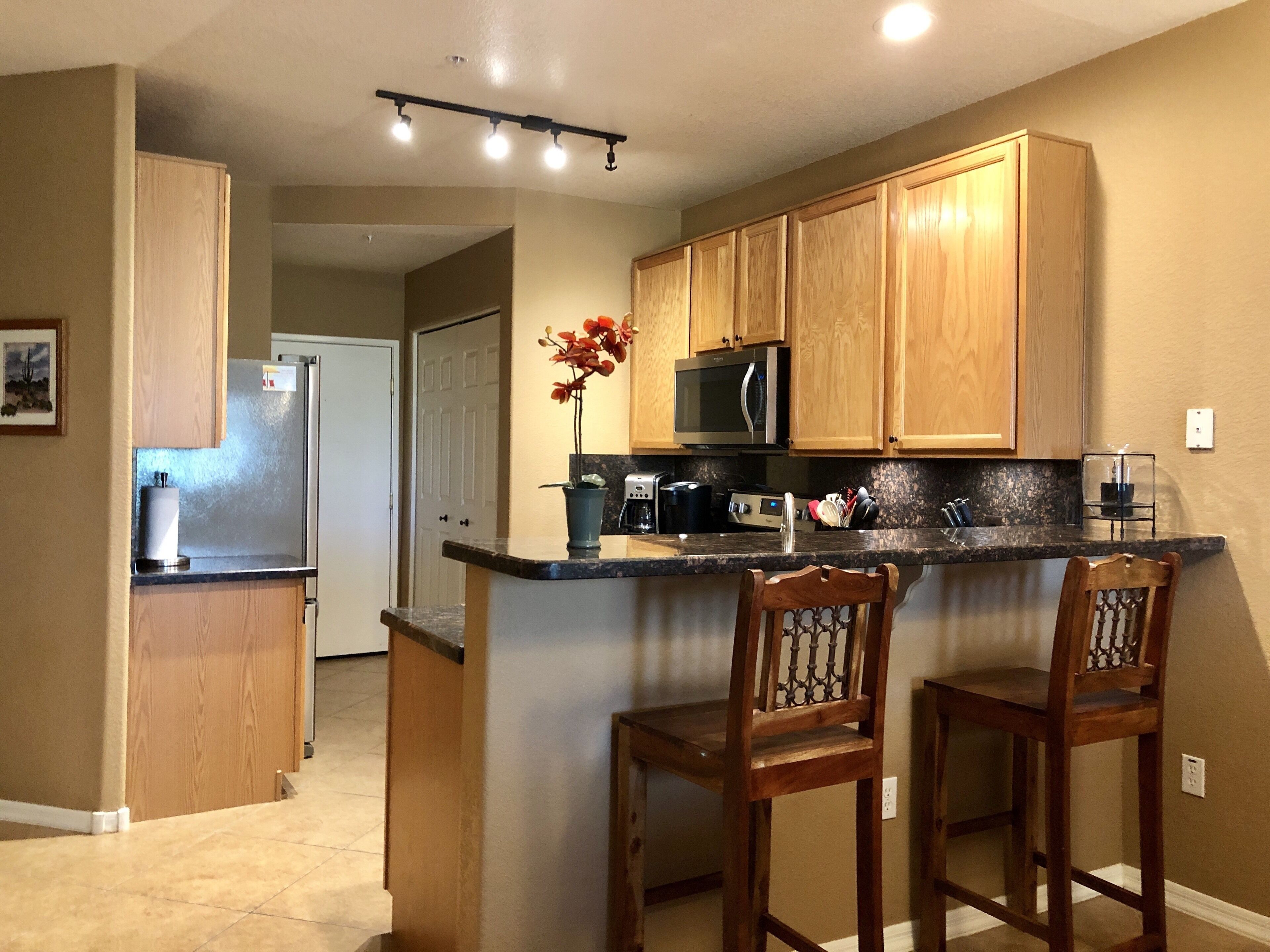 A kitchen with wooden cabinets, a microwave, a coffee maker, and two bar stools.