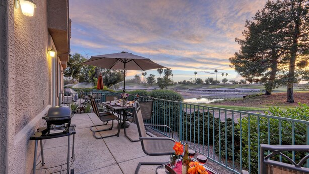An outdoor patio with a grill, tables, and chairs, overlooking a landscaped area with a pond and trees. - SL Lakes Condo w/GOLF VIEWS, Gated Comm w/Htd POOL &Spa, Walk to Mall w/Eats & Theater (Mesa)