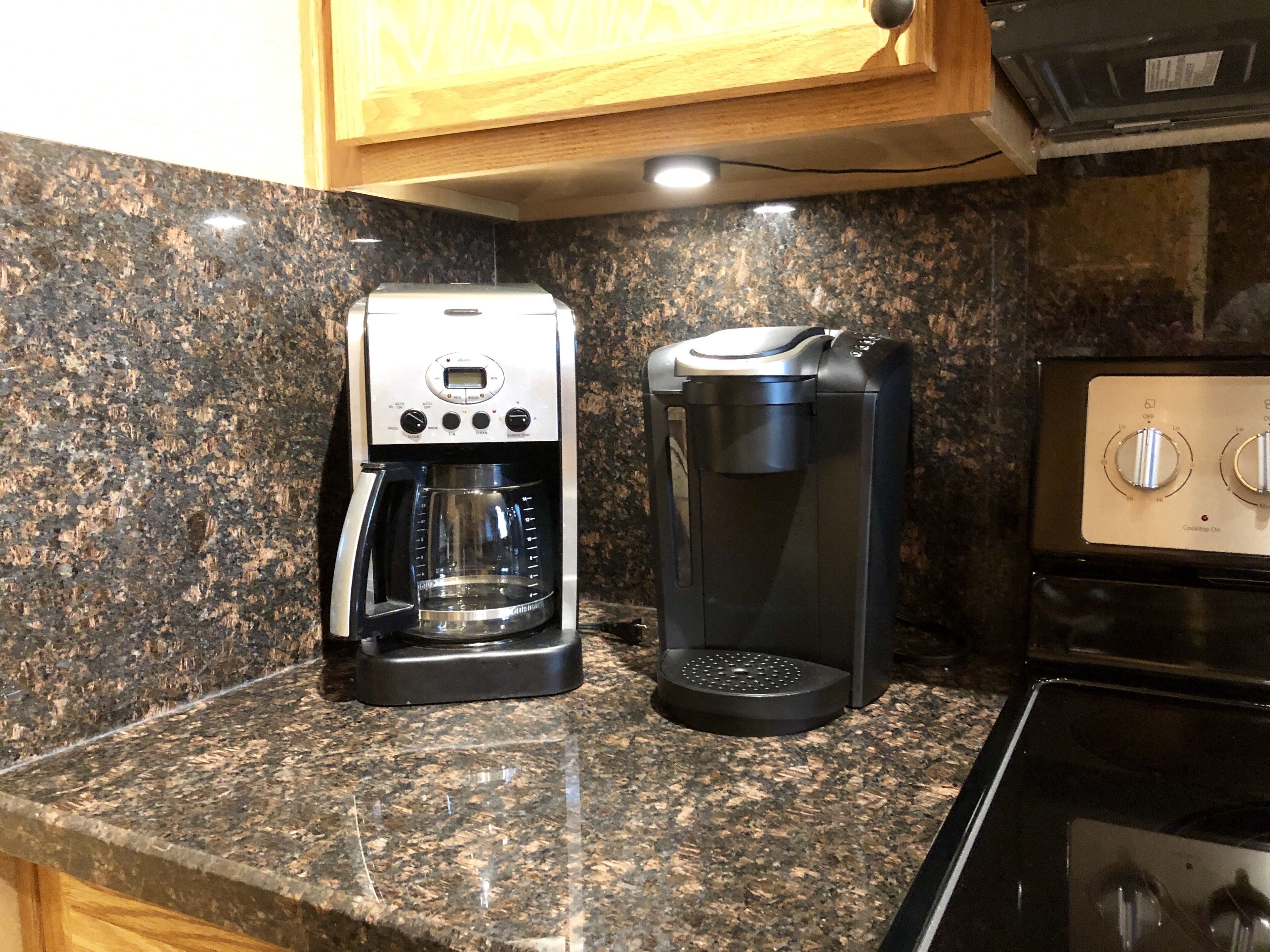 A kitchen with a coffee maker and a coffee pot on a granite countertop.