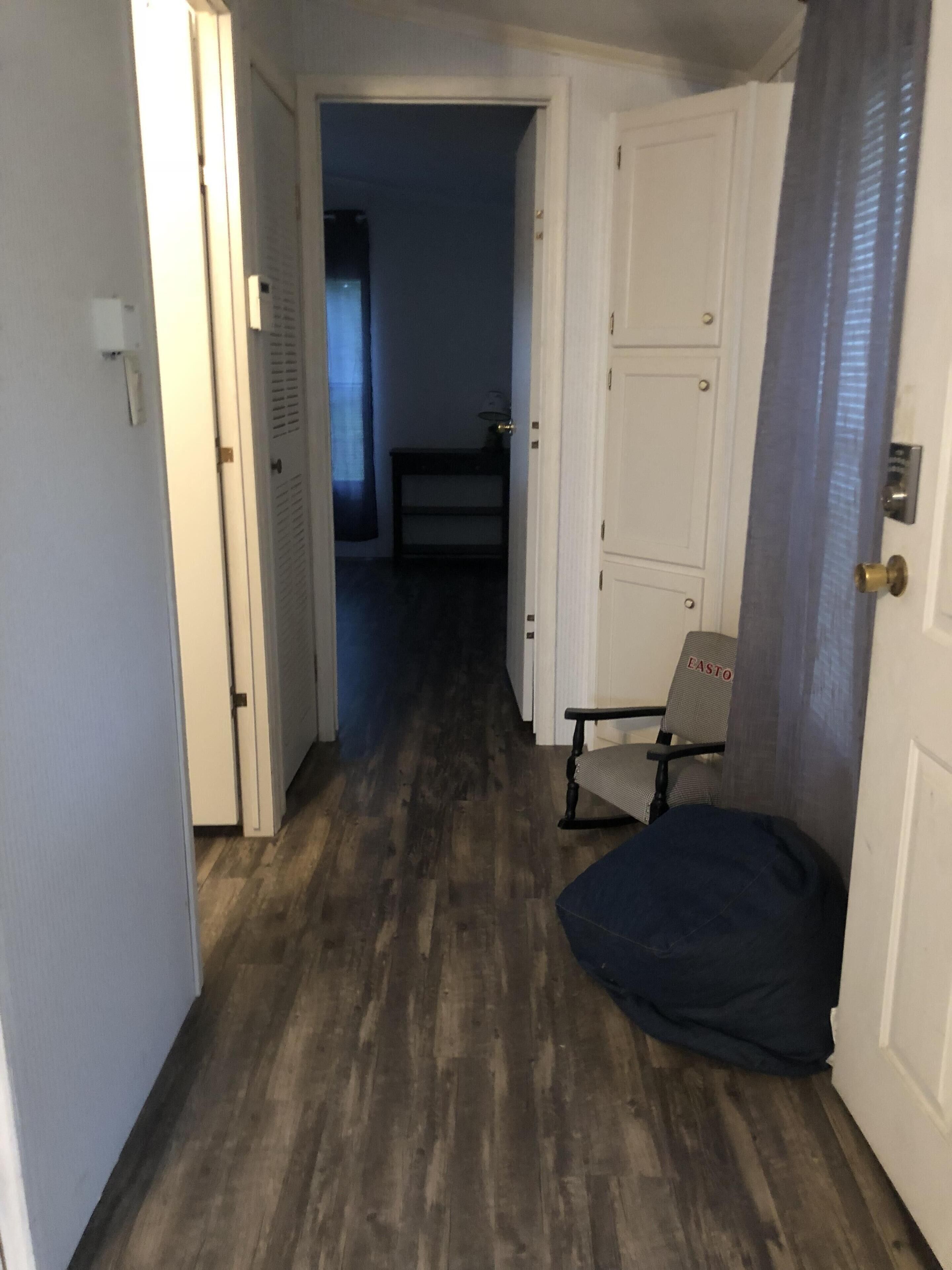 A narrow hallway with wooden flooring, a chair, and a door with a brass handle.