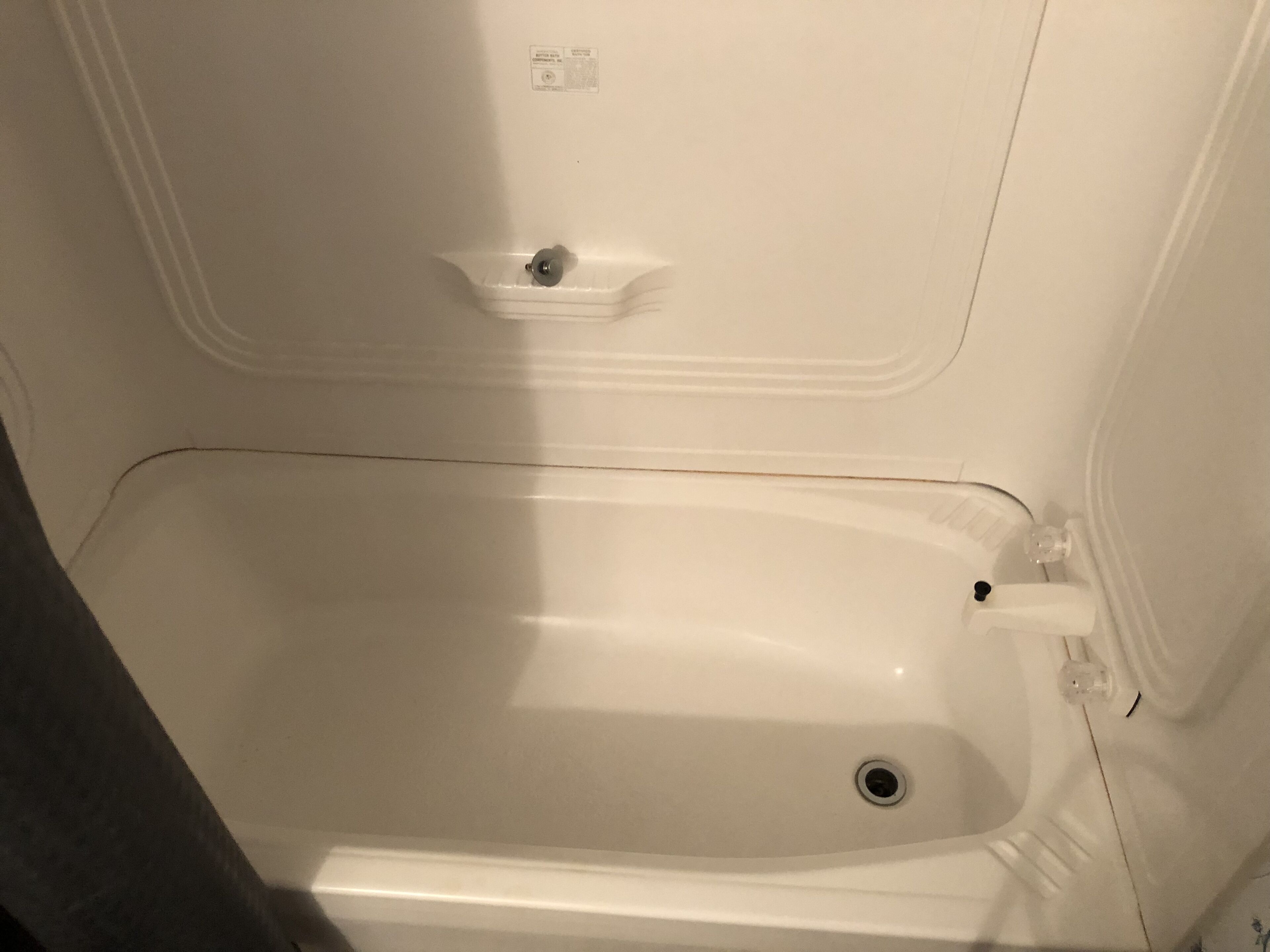 Una bañera blanca con desagüe, grifo y un pequeño estante encima del desagüe.