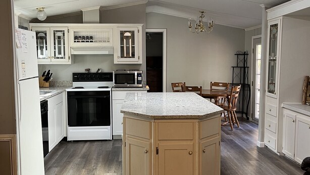 Una cocina moderna con armarios blancos, una isla central y un comedor con candelabro.