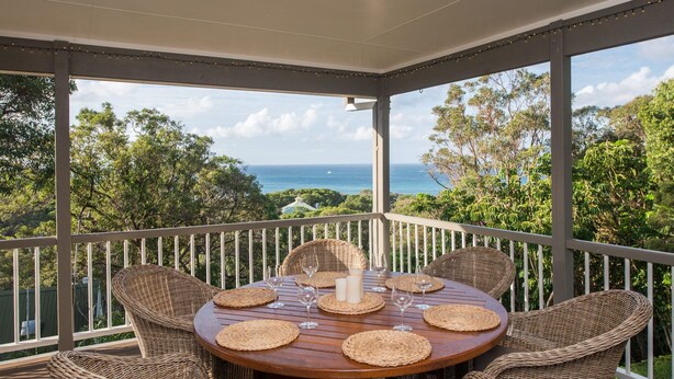 A covered outdoor dining area with wicker furniture and a view of the ocean.