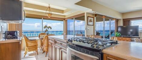 A modern kitchen with a large island, a gas stove, and a view of the ocean.