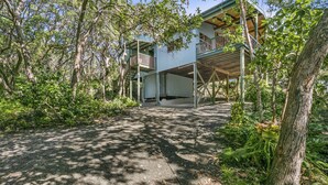 A two-story wooden house with a balcony, surrounded by dense trees and greenery.