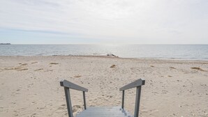 A beach with a wooden walkway leading to the water, a distant pier, and calm sea.