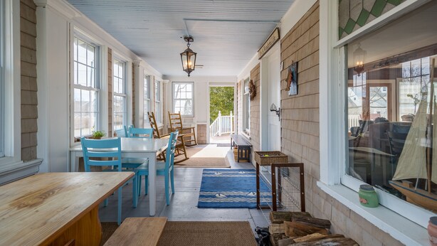 A covered porch with a wooden table and chairs, a blue rug, and a view of the outside.