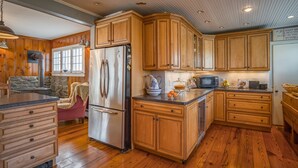 A kitchen with wooden cabinets, a stainless steel refrigerator, a microwave, and a stone fireplace.
