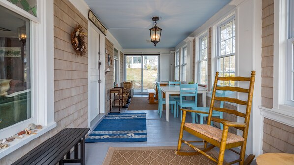 A covered porch with a wooden bench, a rocking chair, and a dining area with blue chairs and a table. - Laurel Beach-Milford (Milford)