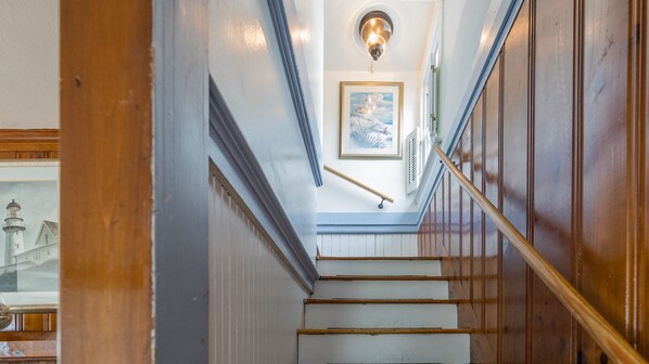 A staircase with wooden handrails and white steps, leading to a landing with a framed picture and a light fixture.