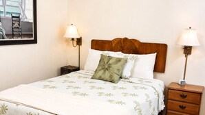 A neatly made bed with a floral bedspread, two bedside lamps, a wooden nightstand, and a framed picture on the wall. - Easy Breezy 2 Bd, 1st Floor, 4 Min to Beach (Isle of Palms)