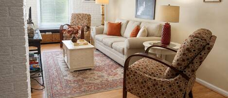 A living room with a sofa, armchair, coffee table, and a patterned rug.