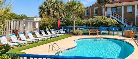 Ein Pool mit Liegestühlen, eine Holzterrasse und ein Gebäude mit rotem Dach im Hintergrund.