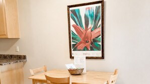 A dining area with a wooden table and chairs, a framed artwork on the wall, and a kitchen counter in the background. - Easy Breezy 2 Bd, 1st Floor, 4 Min to Beach (Isle of Palms)