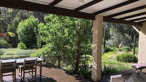 Un espacio al aire libre cubierto con una terraza de madera, una mesa con sillas y un sofá de mimbre.