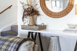 A staircase with a white wall, a round mirror, a vase with dried plants, a wicker basket, and a white trash bin. - Restus Port Fairy ~ Coastal Luxury (Port Fairy)