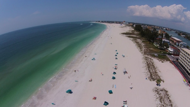 An aerial view of a beach with rows of beach umbrellas and a few people.