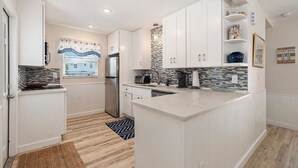 A modern kitchen with white cabinetry, a central island, a backsplash with a mosaic pattern, and a window with blinds.