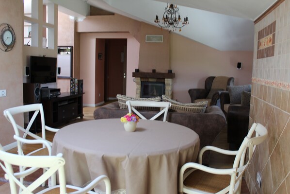 A living room with a round table, white chairs, a fireplace, and a television.